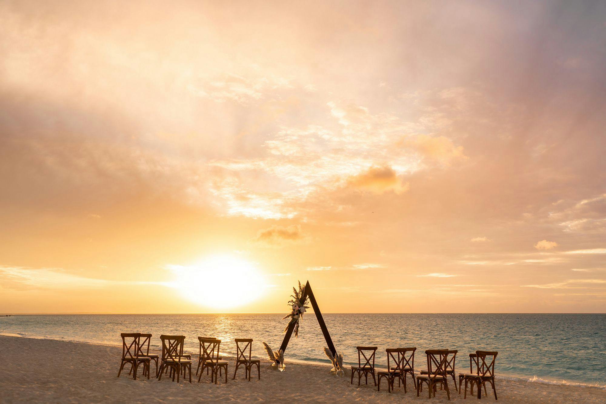 Boho beachside ceremony with triangular wedding arch at The Ritz-Carlton Turks & Caicos | PartySlate